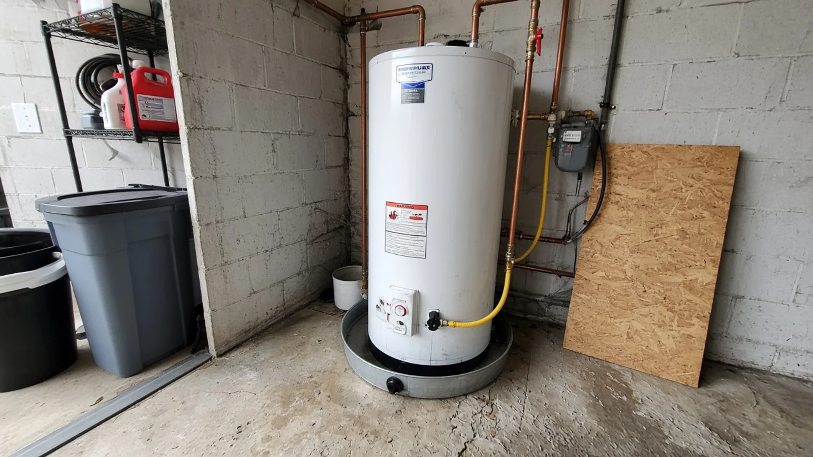 White water heater in a garage corner with copper pipes