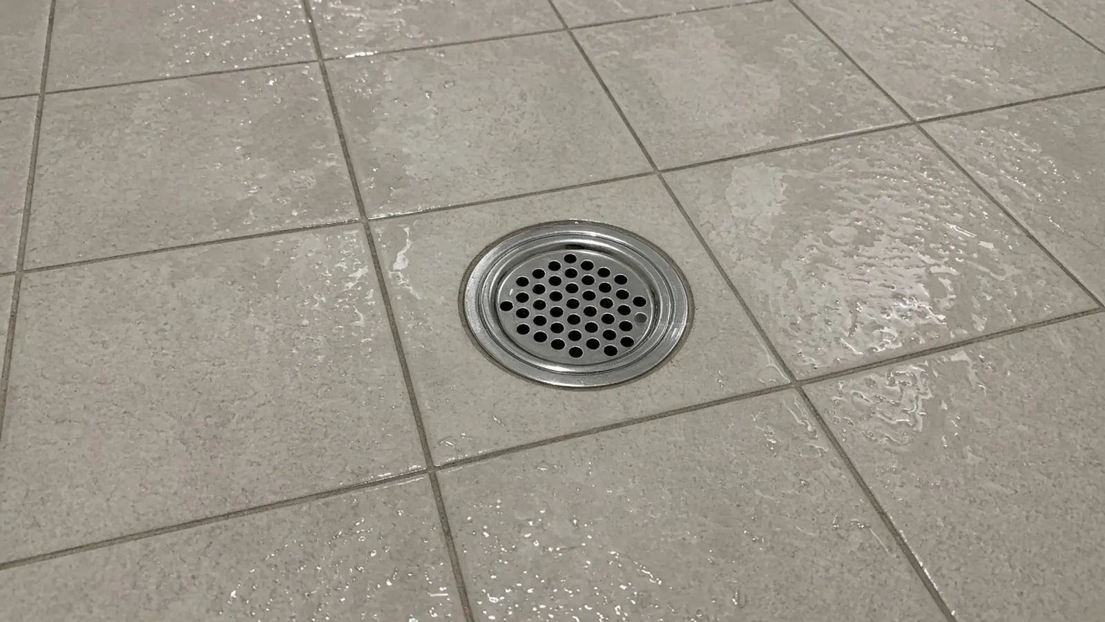 Chrome floor drain grate on a tiled bathroom floor